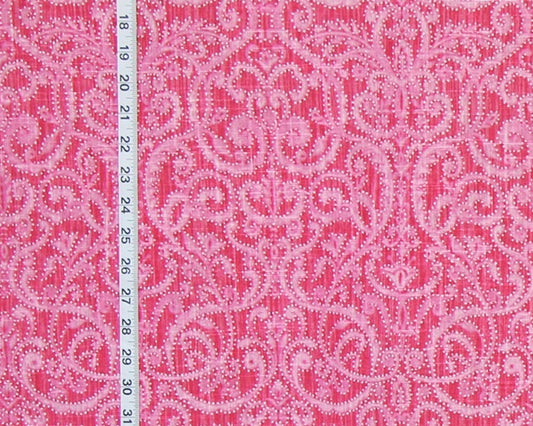 A close-up of a pink patterned fabric with a light pink ornamental damask design, shown next to a white ruler for scale.