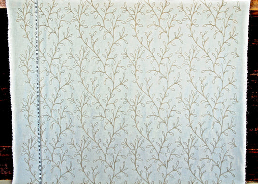 A close-up of a white fabric with a repeating beige embroidered vine or branch pattern, shown flat against a dark background.