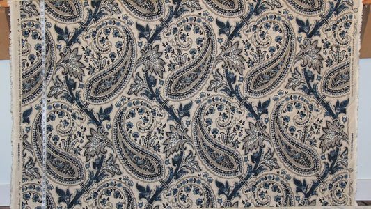 A close-up of a fabric or wallpaper sample featuring a classic navy blue and beige paisley pattern, with a white measuring tape visible along the left edge.