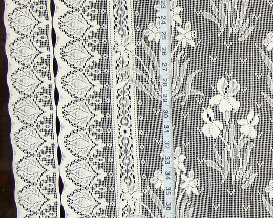 White floral lace fabric with multiple decorative borders and a measuring tape laid vertically to show scale.