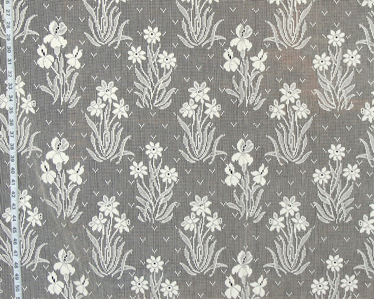 Gray and white floral lace fabric with a repeating iris pattern, shown flat with a measuring tape visible along the left edge.