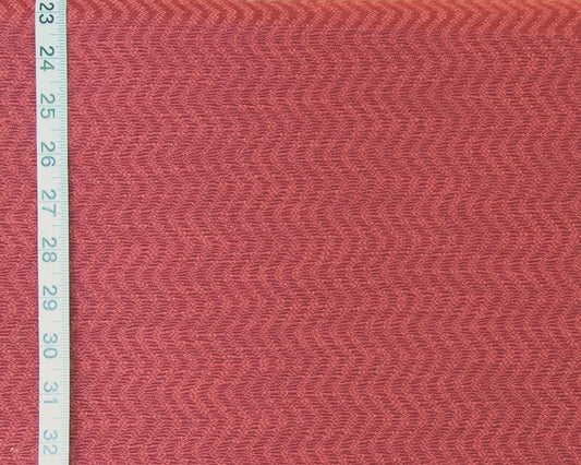 A close-up of textured fabric in a muted dusty rose or mauve pink color, shown with a white measuring tape along the left edge for scale.