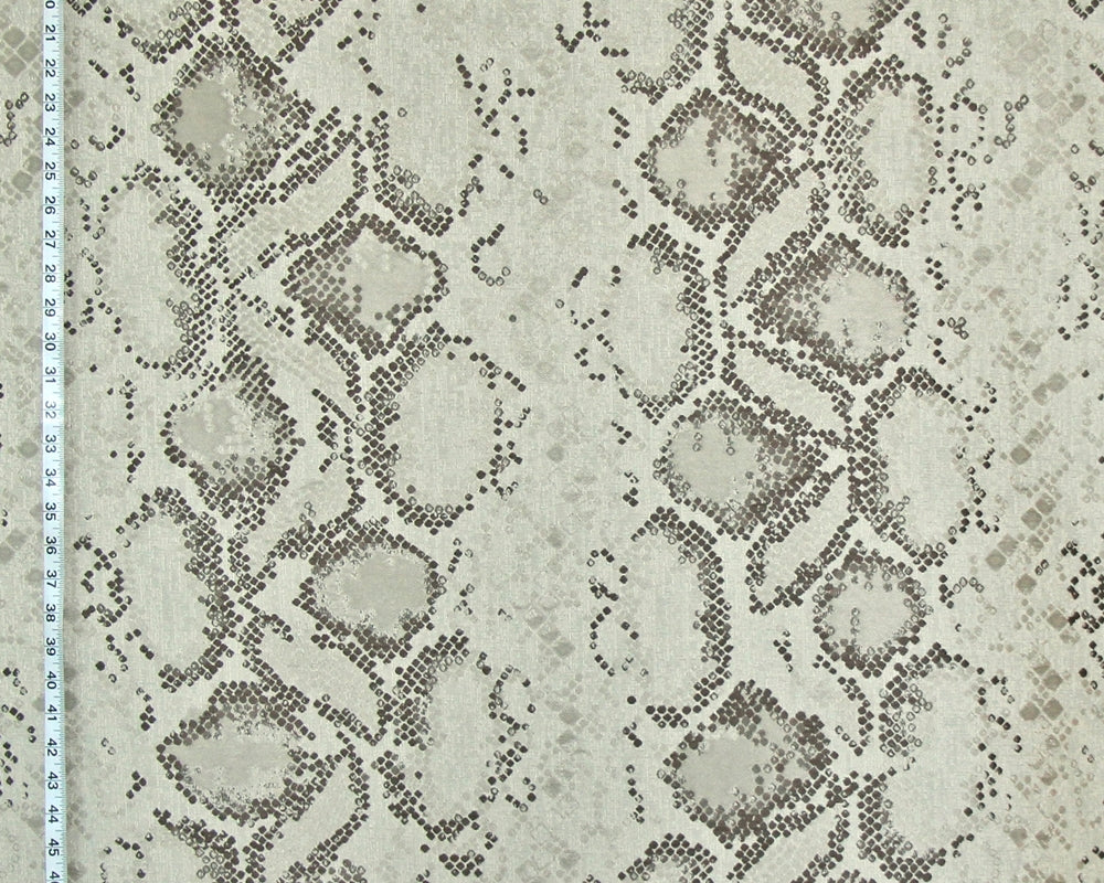 A close-up of a fabric or wallpaper pattern featuring a snakeskin design in beige, gray, and brown tones, with a white ruler visible along the left edge for scale.