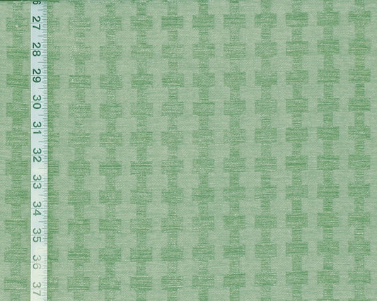 A close-up of a light green fabric with a repeating tonal geometric pattern, shown with a white measuring ruler along the left edge for scale.