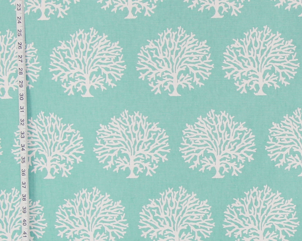 A close-up of a fabric pattern featuring repeating white coral tree motifs on a light aqua background, with a measuring tape visible along the left edge.