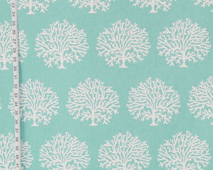 A close-up of a fabric pattern featuring repeating white coral tree motifs on a light aqua background, with a measuring tape visible along the left edge.