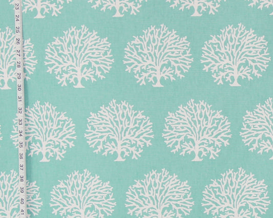 A close-up of a fabric pattern featuring repeating white coral tree motifs on a light aqua background, with a measuring tape visible along the left edge.