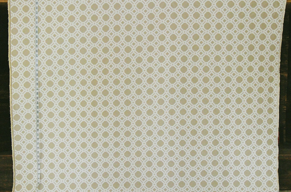 A close-up of a fabric or wallpaper pattern featuring a repeating geometric trellis design in beige and off-white, with a visible ruler scale on the left edge.