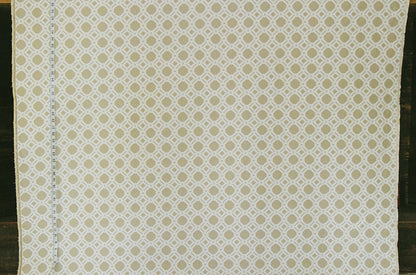 A close-up of a fabric or wallpaper pattern featuring a repeating geometric trellis design in beige and off-white, with a visible ruler scale on the left edge.