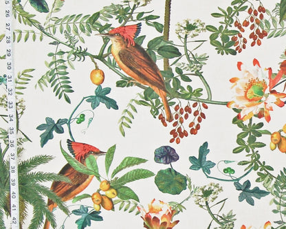 A close-up of a botanical and bird print fabric featuring two red-crowned woodpeckers among green leaves, yellow berries, and white flowers on an off-white background, with a measuring tape visible along the left edge.