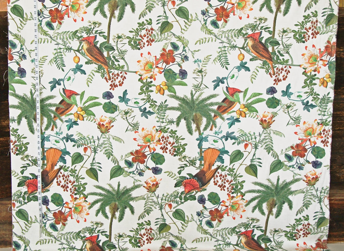 A close-up of a fabric or wallpaper pattern featuring tropical birds, palm trees, and flowers on a white background, photographed flat against a dark wood surface.