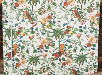 A close-up of a fabric or wallpaper pattern featuring tropical birds, palm trees, and flowers on a white background, photographed flat against a dark wood surface.