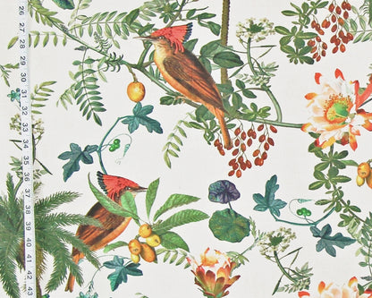 A close-up of a botanical fabric pattern featuring two red-crowned birds perched among green leaves, yellow berries, and orange flowers on an off-white background, with a measuring tape visible along the left edge.