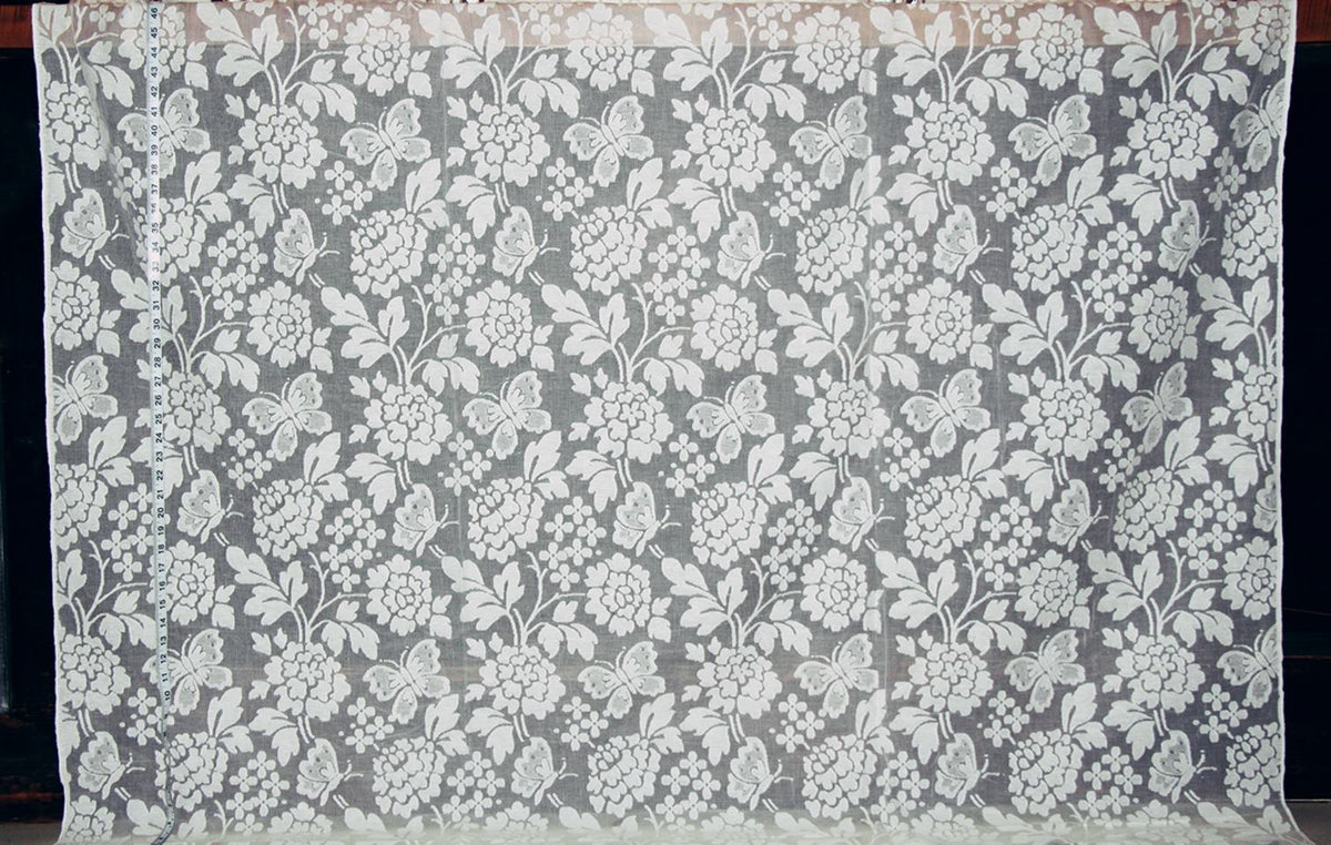 A rectangular piece of sheer white floral lace fabric with a repeating embroidered or printed floral pattern, displayed flat against a dark background.