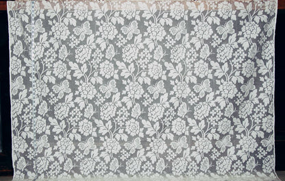 A rectangular piece of sheer white floral lace fabric with a repeating embroidered or printed floral pattern, displayed flat against a dark background.