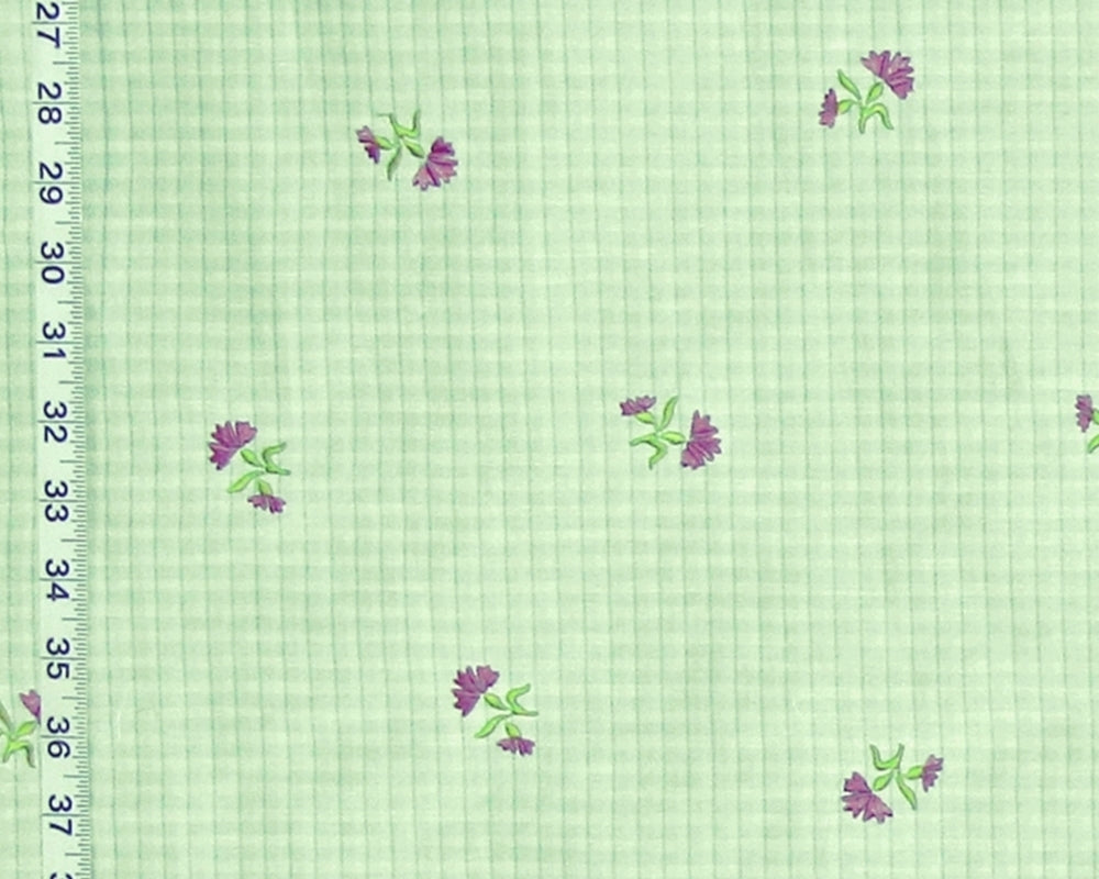 Light green gingham fabric with a repeating pattern of small purple flowers with green leaves, shown with a white ruler on the left edge for scale.