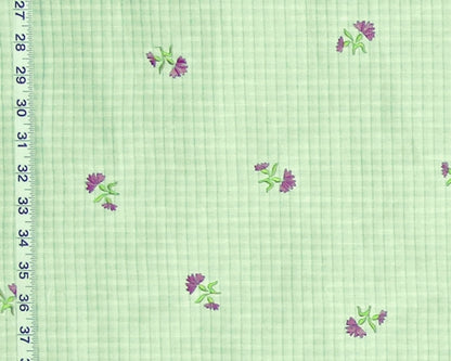 Light green gingham fabric with a repeating pattern of small purple flowers with green leaves, shown with a white ruler on the left edge for scale.