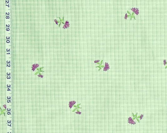 Light green gingham fabric with a repeating pattern of small purple flowers with green leaves, shown with a white ruler on the left edge for scale.