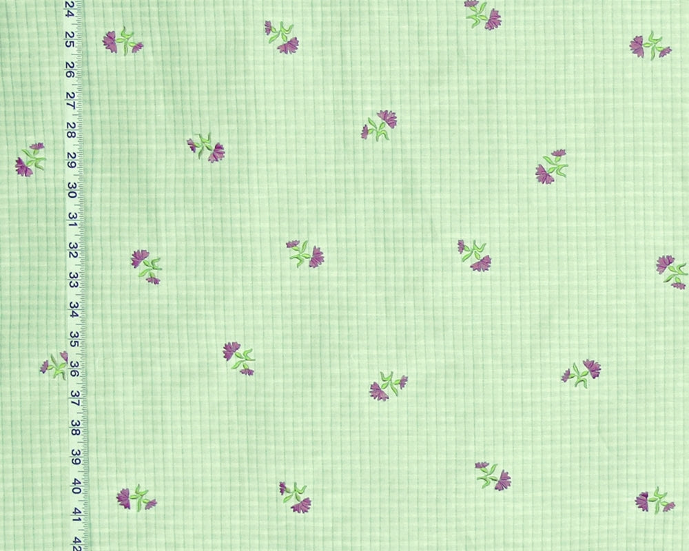Light green gingham fabric with a repeating pattern of small purple flowers and green leaves, shown with a black ruler on the left edge for scale.
