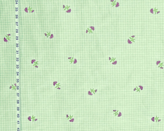 Light green gingham fabric with a repeating pattern of small purple flowers and green leaves, shown with a black ruler on the left edge for scale.