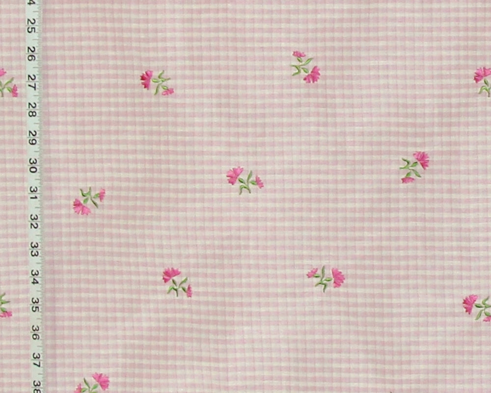 Pink and white gingham fabric with small pink flowers and green leaves, shown with a measuring tape along the left edge.