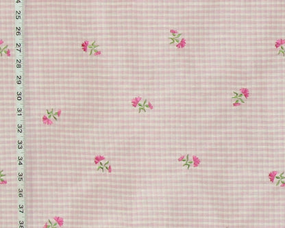 Pink and white gingham fabric with small pink flowers and green leaves, shown with a measuring tape along the left edge.
