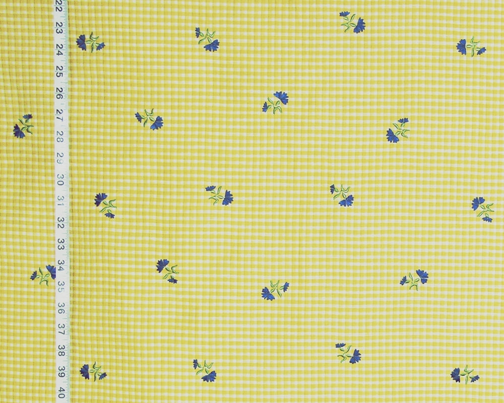 Yellow and white gingham fabric with small blue and green floral motifs, shown with a white ruler on the left side for scale.