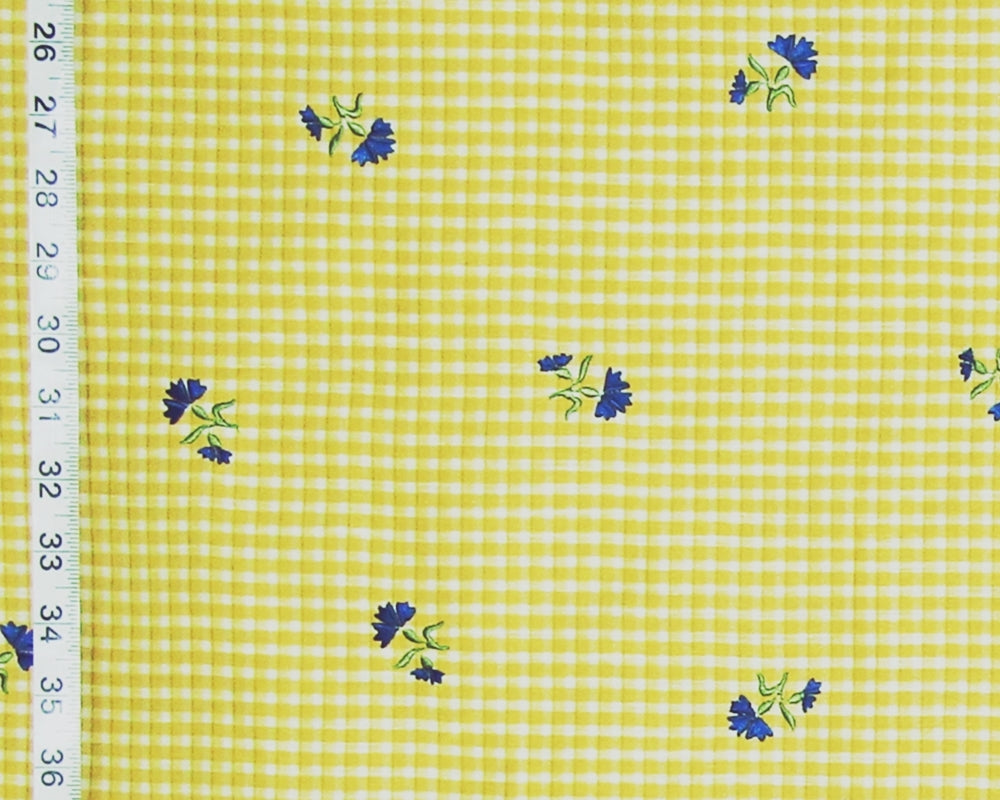Yellow and white gingham fabric with small blue and green floral motifs, shown with a measuring tape along the left edge.