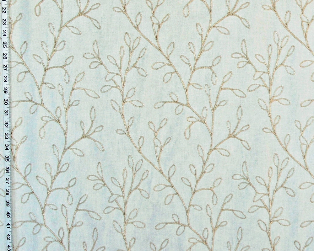 A close-up of a light blue fabric with a repeating pattern of delicate beige leafy vines, with a black measurement ruler visible along the left edge.