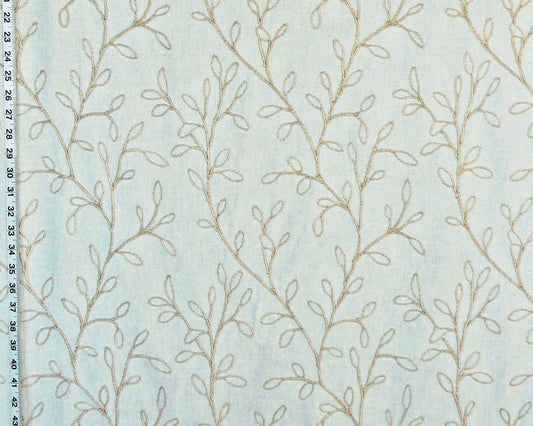 A close-up of a light blue fabric with a repeating pattern of delicate beige leafy vines, with a black measurement ruler visible along the left edge.
