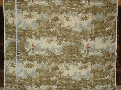 Textile with landscape design featuring figures and trees, displayed on a wooden surface.