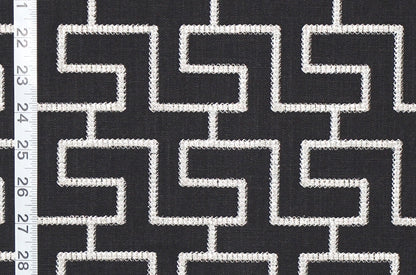 Black and white geometric patterned fabric with a repeating maze-like line design, shown close up with a white ruler on the left edge for scale.