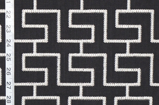 Black and white geometric patterned fabric with a repeating maze-like line design, shown close up with a white ruler on the left edge for scale.