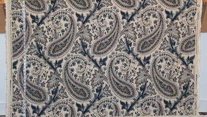 A close-up of a fabric or wallpaper sample featuring a classic navy blue and beige paisley pattern, with a white measuring tape visible along the left edge.
