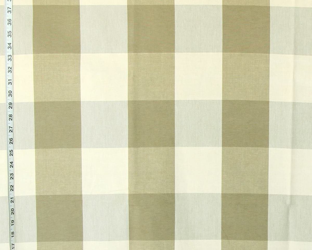 A close-up of a fabric surface with a large-scale gingham plaid pattern in muted olive green and off-white, with a measuring tape visible along the left edge.