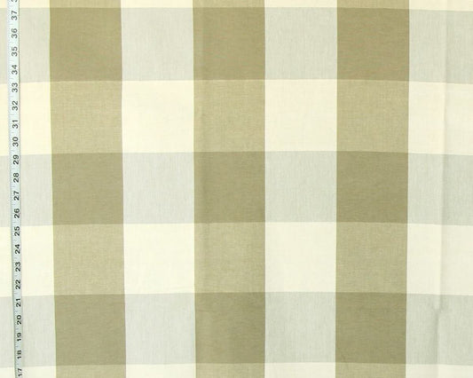 A close-up of a fabric surface with a large-scale gingham plaid pattern in muted olive green and off-white, with a measuring tape visible along the left edge.