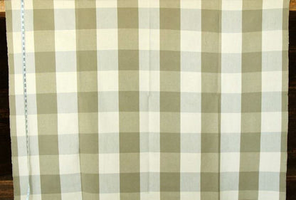 A close-up of a fabric with a gingham check pattern in sage green and off-white, laid flat on a dark wooden surface with a measuring tape visible on the left edge.