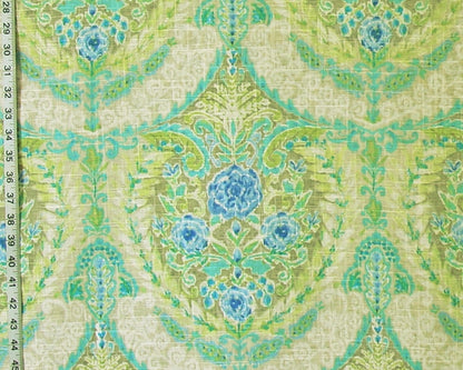 A close-up of a patterned fabric with a repeating damask-style floral design in light green, turquoise, and blue on a warm beige background. A measuring ruler is visible along the left edge to show scale.