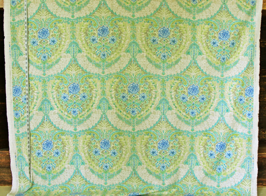 A close-up of a patterned fabric with a repeating scalloped damask design in light green, mint, cream, and blue, with a white stitched border on the left side.