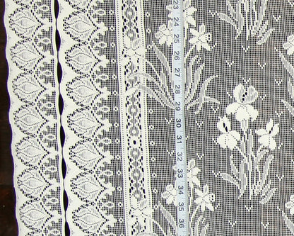 White floral lace fabric with multiple decorative borders and a measuring tape laid vertically to show scale.