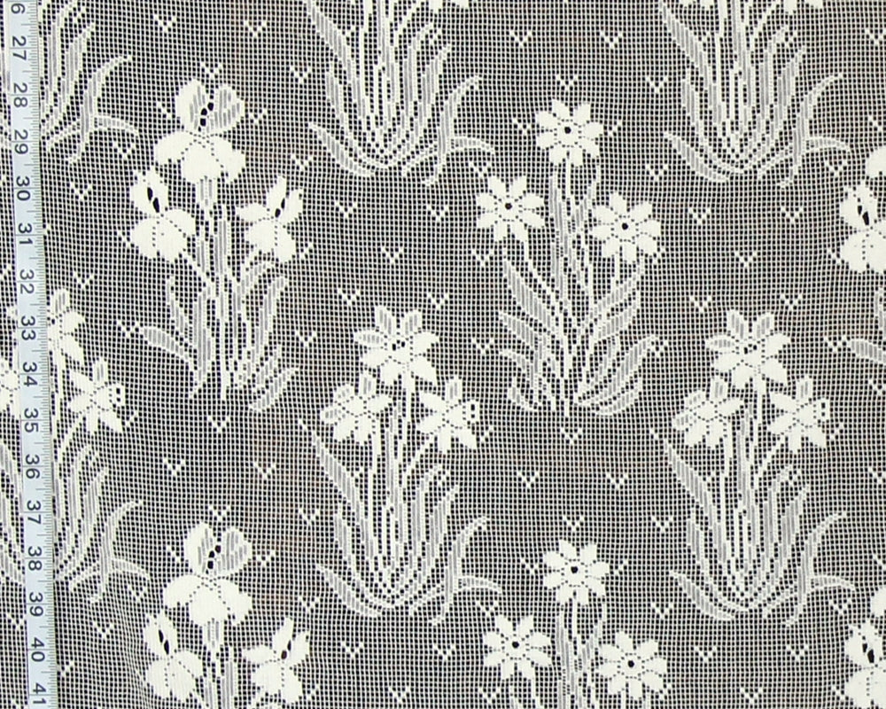 White floral lace fabric with a repeating pattern of iris flowers and leaves on a gray mesh background, shown with a measuring tape along the left edge.