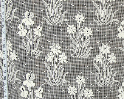 White floral lace fabric with a repeating pattern of iris flowers and leaves on a gray mesh background, shown with a measuring tape along the left edge.