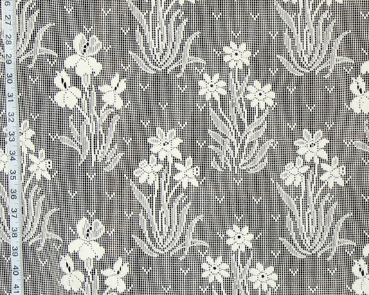 White floral lace fabric with a repeating pattern of iris flowers and leaves on a gray mesh background, shown with a measuring tape along the left edge.
