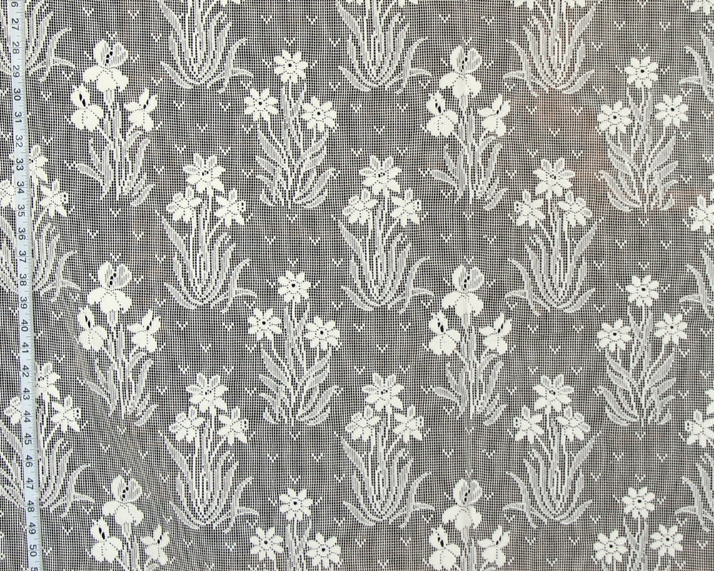 Gray and white floral lace fabric with a repeating iris pattern, shown flat with a measuring tape visible along the left edge.