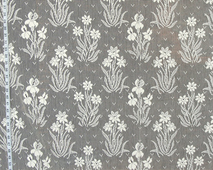 Gray and white floral lace fabric with a repeating iris pattern, shown flat with a measuring tape visible along the left edge.