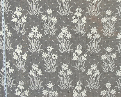 Gray and white floral patterned fabric with a repeating iris-like motif, shown close up with a measuring tape along the left edge.