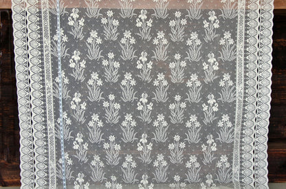 A square lace tablecloth with a delicate white floral pattern on a sheer gray background, finished with an intricate scalloped lace border.