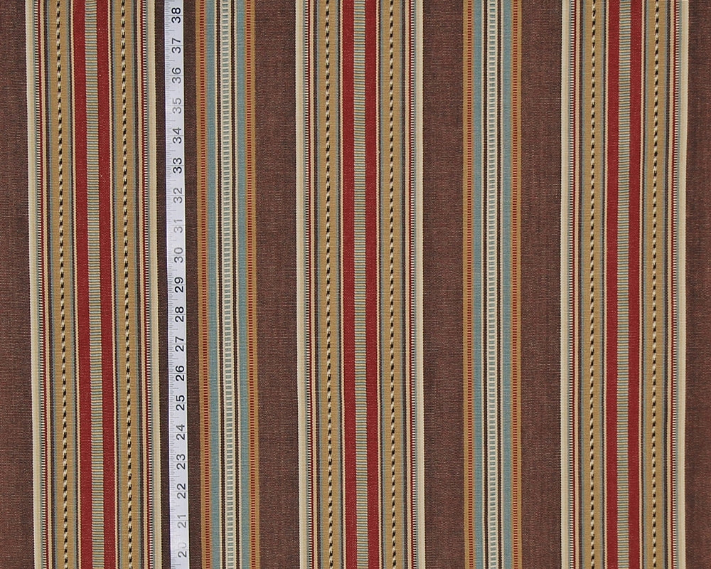 A close-up of a striped fabric pattern with vertical bands in brown, rust red, beige, and muted blue, with a white measuring tape running down the center to indicate scale.