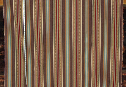 A close-up of a striped textile or fabric panel with vertical bands in brown, beige, red, and muted blue, with a measuring tape visible along the left side.