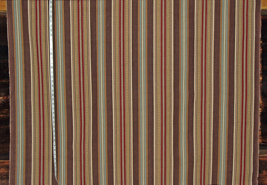 A close-up of a striped textile or fabric panel with vertical bands in brown, beige, red, and muted blue, with a measuring tape visible along the left side.